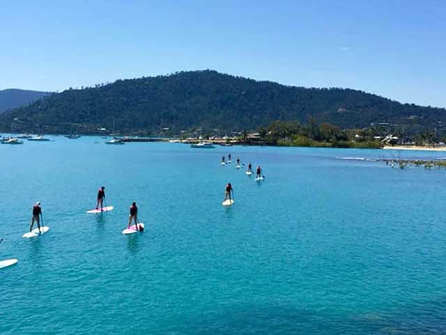 Group of friends stand up paddle boarding in Airlie Beach